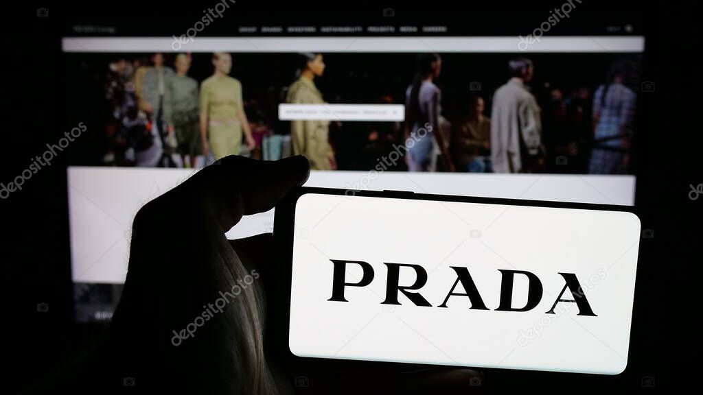 Stuttgart, Germany - 05-17-2025: Person holding mobile phone with logo of luxury fashion house company Prada S.p.A. on screen in front of web page. Focus on phone display.