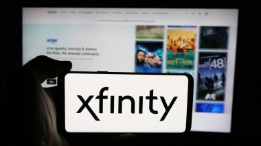 Stuttgart, Almanya - 05-18-2025: İnternet sayfası önünde Comcast Cable Communications LLLC (Xfinity) logosu olan cep telefonu sahibi kişi. Telefon ekranına odaklan.