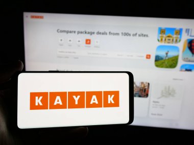 Stuttgart, Almanya - 05-18-2025: İnternet sitesinin önünde ekranda ABD 'li seyahat metasearch şirketi Kayak' ın logosuna sahip akıllı telefonu tutan kişi. Telefon ekranına odaklan.