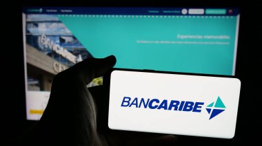Stuttgart, Almanya - 05-18-2025: Banco del Caribe C.A. şirketinin logosuna sahip cep telefonu sahibi kişi (Bancaribe) Web sayfasının önünde ekranda. Telefon ekranına odaklan.