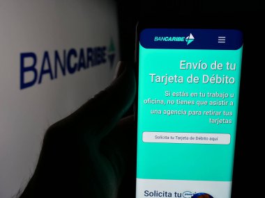 Stuttgart, Almanya - 05-18-2025: Banco del Caribe C.A. şirketinin internet sayfası ile akıllı telefon tutan kişi Logonun önündeki ekranda (Bancaribe). Telefon ekranının merkezine odaklan.