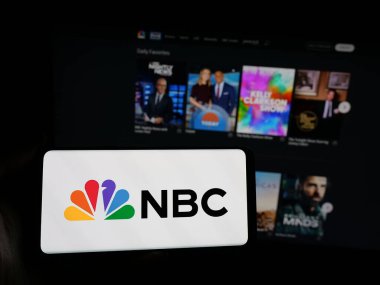 Stuttgart, Almanya - 05-25-2025: İnternet sitesi önünde Ulusal Yayın Şirketi 'nin (NBC) logosuna sahip akıllı telefonu elinde tutan kişi. Telefon ekranına odaklan.