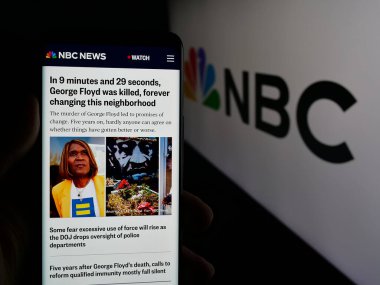 Stuttgart, Almanya - 05-25-2025: Ulusal Yayın Şirketi 'nin (NBC) web sayfası olan akıllı telefonu logo önünde ekranda tutan kişi. Telefon ekranının merkezine odaklan.