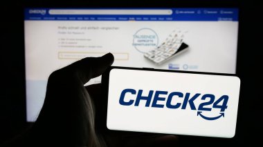 Stuttgart, Almanya - 05-25-2025: Alman fiyat karşılaştırma şirketi Check24 GmbH logosuna sahip cep telefonu sahibi kişi web sayfasının önünde ekranda. Telefon ekranına odaklan.