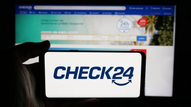 Stuttgart, Almanya - 05-25-2025: Üzerinde Alman fiyat karşılaştırma şirketi Check24 GmbH logosu olan cep telefonu sahibi kişi web sayfasının önünde ekranda. Telefon ekranına odaklan.