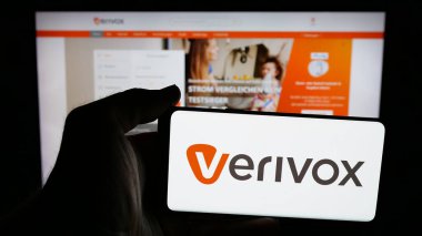 Stuttgart, Almanya - 05-25-2025: Üzerinde Alman fiyat karşılaştırma şirketi Verivox GmbH logosu bulunan cep telefonu sahibi kişi web sayfasının önünde ekranda. Telefon ekranına odaklan.