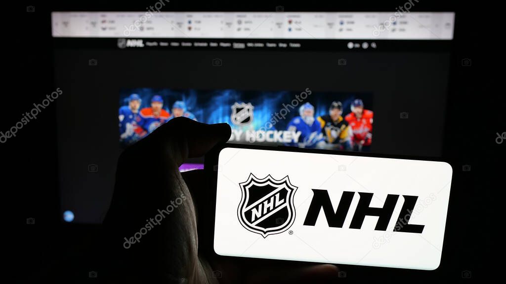 Stuttgart, Germany - 05-18-2025: Person holding mobile phone with logo of National Hockey League (NHL) on screen in front of web page. Focus on phone display.