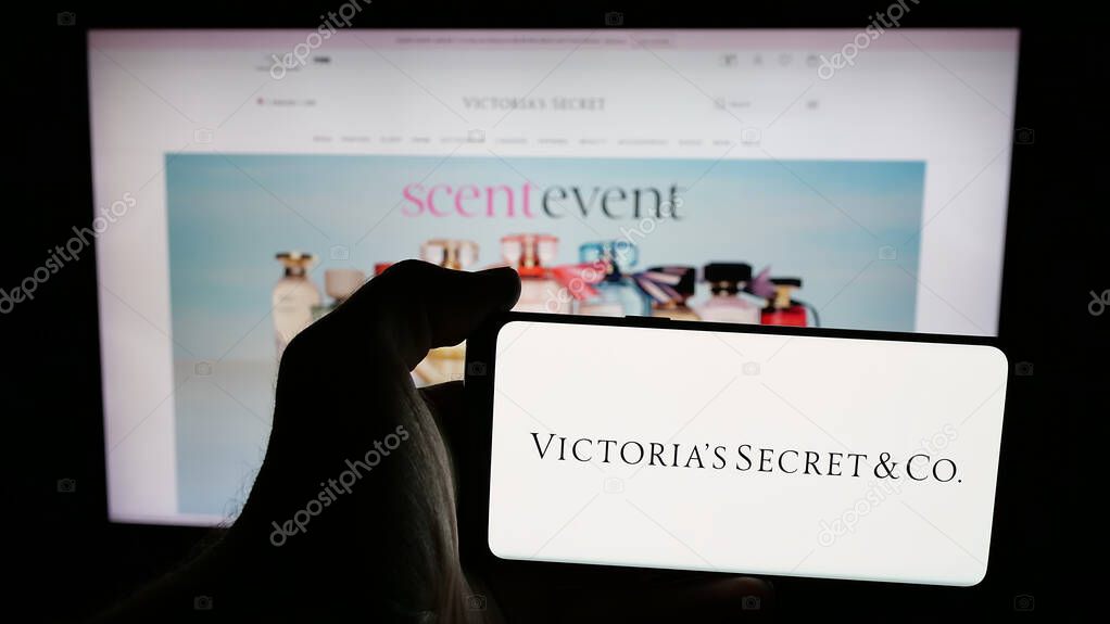 Stuttgart, Germany - 05-18-2025: Person holding mobile phone with logo of US lingerie company Victoria's Secret Co. on screen in front of web page. Focus on phone display.