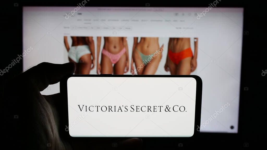 Stuttgart, Germany - 05-18-2025: Person holding cellphone with logo of US lingerie company Victoria's Secret Co. on screen in front of webpage. Focus on phone display.