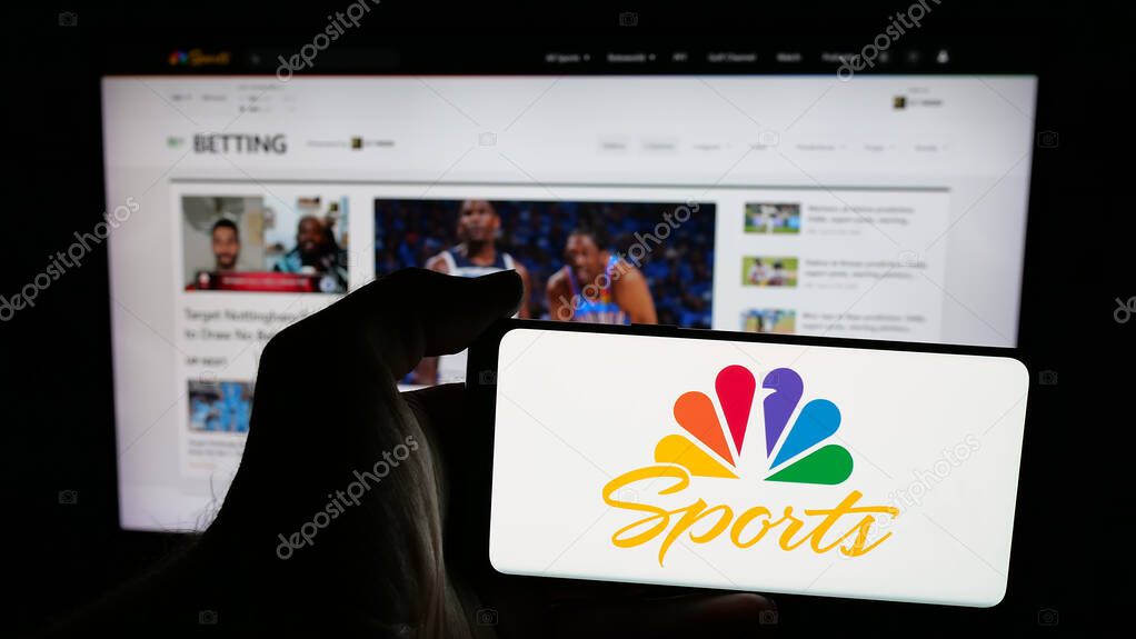 Stuttgart, Germany - 05-25-2025: Person holding mobile phone with logo of US television channel NBC Sports (NBCSports) on screen in front of web page. Focus on phone display.