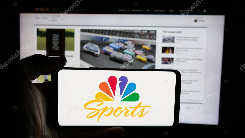 Stuttgart, Germany - 05-25-2025: Person holding cellphone with logo of US television channel NBC Sports (NBCSports) on screen in front of webpage. Focus on phone display.