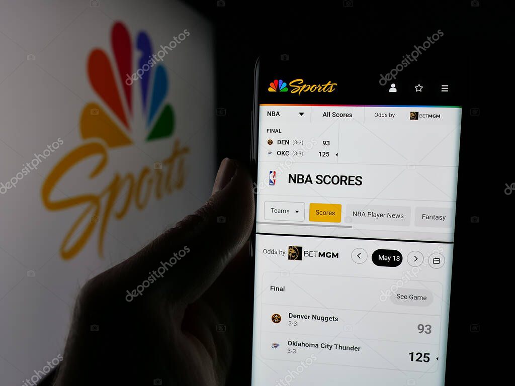 Stuttgart, Germany - 05-25-2025: Person holding smartphone with web page of US television channel NBC Sports (NBCSports) on screen in front of logo. Focus on center of phone display.