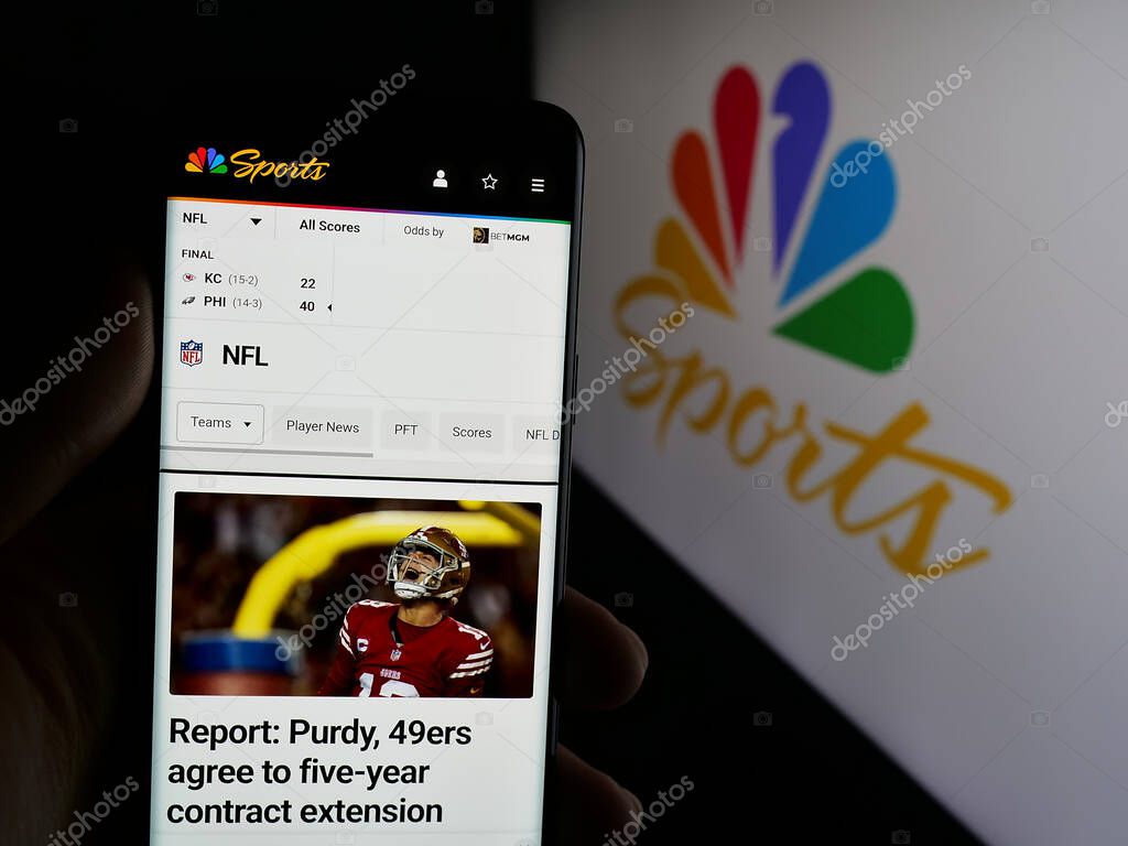Stuttgart, Germany - 05-25-2025: Person holding cellphone with webpage of US television channel NBC Sports (NBCSports) on screen in front of logo. Focus on center of phone display.