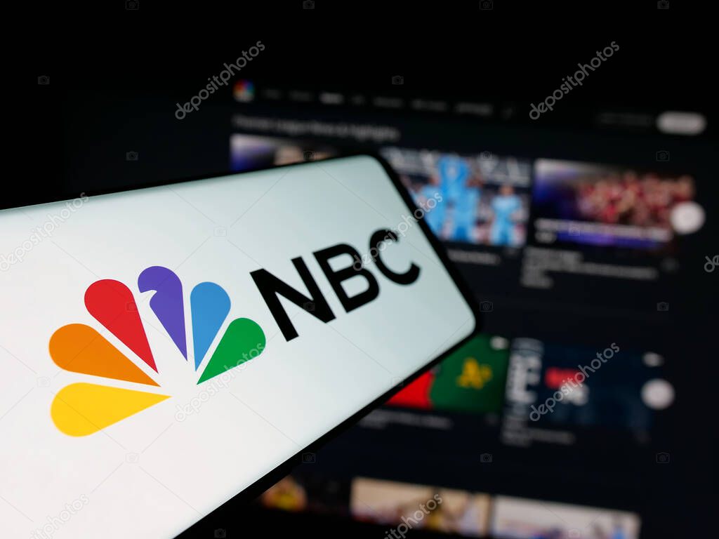 Stuttgart, Germany - 05-25-2025: Smartphone with logo of network National Broadcasting Company (NBC) on screen in front of website. Focus on center-left of phone display.