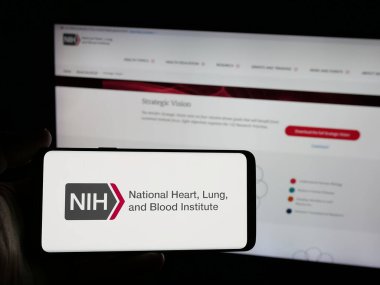 Stuttgart, Almanya - 05-25-2025: İnternet sitesinin önünde ABD Sağlık Enstitüsü NHLBI logosu olan akıllı telefon sahibi kişi. Telefon ekranına odaklan.