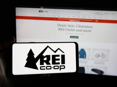 Stuttgart, Almanya - 05-25-2025: Web sitesi önünde ekranda, üzerinde Amerikan şirketinin logosu bulunan akıllı telefon sahibi kişi. (REI) Telefon ekranına odaklan.