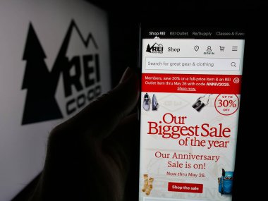 Stuttgart, Almanya - 05-25-2025: Logonun önünde ekranda, ABD 'li bir şirketin eğlence amaçlı ekipman şirketinin web sayfası ile akıllı telefon bulunduran kişi. (REI) Telefon ekranının merkezine odaklan.