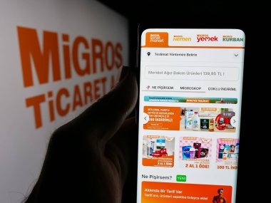 Stuttgart, Almanya - 05-25-2025: Cep telefonu sahibi İsviçreli süpermarket şirketi Migros 'un internet sayfası logo önünde ekranda. Telefon ekranının merkezine odaklan.