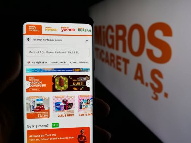 Stuttgart, Almanya - 05-25-2025: İsviçreli süpermarket şirketi Migros 'un web sayfası logonun önünde duran kişi. Telefon ekranının merkezine odaklan.