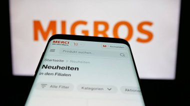 Stuttgart, Almanya - 05-25-2025: İsviçreli süpermarket şirketi Migros 'un web sitesiyle birlikte logo önünde cep telefonu. Telefon ekranının sol üst kısmına odaklan.