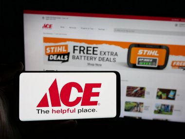 Stuttgart, Almanya - 05-25-2025: ABD 'li perakende şirketi Ace Hardware Corporation' ın logosunu elinde bulunduran kişi web sitesinin önünde ekranda. Telefon ekranına odaklan.