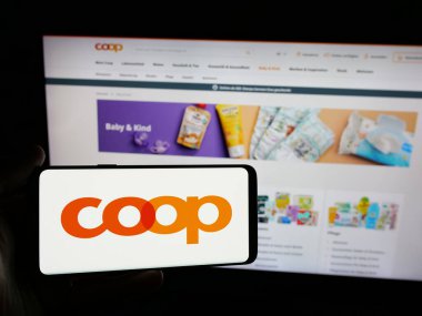 Stuttgart, Almanya - 05-26-2025: Üzerinde İsviçreli perakende şirketi Coop Genossenschaft 'ın logosu olan akıllı telefonu web sitesi önünde tutan kişi. Telefon ekranına odaklan.