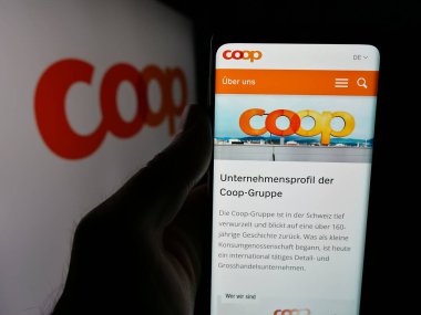 Stuttgart, Almanya - 05-26-2025: Cep telefonunda İsviçreli perakende şirketi Coop Genossenschaft 'ın web sayfası bulunan kişi logonun önünde ekranda. Telefon ekranının merkezine odaklan.