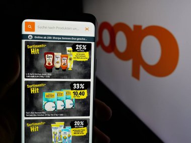 Stuttgart, Almanya - 05-26-2025: İsviçreli perakende şirketi Coop Genossenschaft 'ın web sayfası ile akıllı telefon sahibi kişi logonun önünde ekranda. Telefon ekranının merkezine odaklan.