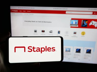 Stuttgart, Almanya - 05-26-2025: İnternet sitesinin önünde ekranda ABD 'li ofis malzemeleri perakende şirketi Staples Inc.' in logosuna sahip akıllı telefonu tutan kişi. Telefon ekranına odaklan.