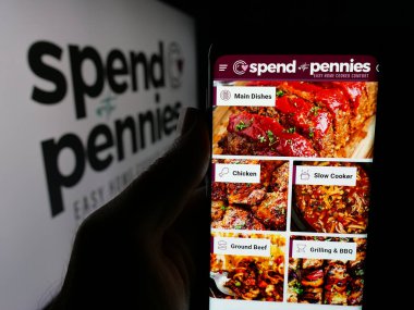 Stuttgart, Almanya - 05-26-2025: Logo önündeki ekranda, şirket tarafından Harcanan Kuruşlarla Harcama (SWP Media Ltd.) web sayfası olan akıllı telefon sahibi kişi. Telefon ekranının merkezine odaklan.