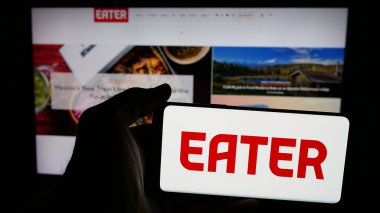Stuttgart, Almanya - 05-26-2025: İnternet sayfası önünde ekranda ABD 'li gıda şirketi Eater' ın (Eater.com) logosunun bulunduğu cep telefonu sahibi kişi. Telefon ekranına odaklan.