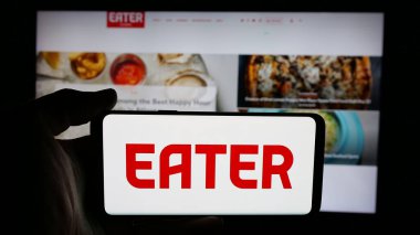 Stuttgart, Almanya - 05-26-2025: İnternet sayfası önünde ABD 'li gıda şirketi Eater' ın (Eater.com) logosuna sahip cep telefonu sahibi kişi. Telefon ekranına odaklan.