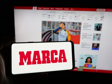 Stuttgart, Almanya - 05-27-2025: İnternet sitesinin önünde üzerinde İspanyol günlük spor gazetesi Marca 'nın logosu bulunan akıllı telefon sahibi kişi. Telefon ekranına odaklan.