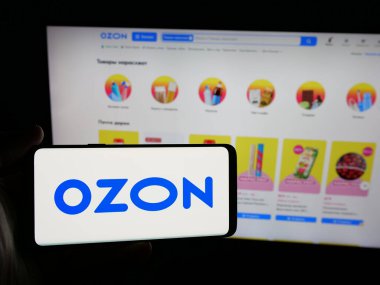 Stuttgart, Almanya - 05-27-2025: İnternet sitesinin önünde Rus e-ticaret şirketi Özon 'un (Özon.ru) logosuna sahip akıllı telefonu elinde tutan kişi. Telefon ekranına odaklan.