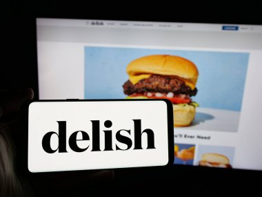 Stuttgart, Almanya - 05-27-2025: İnternet sitesi önünde ekranda ABD gıda çevrimiçi dergisi Delish.com 'un (Hearst) logosuna sahip akıllı telefon tutan kişi. Telefon ekranına odaklan.
