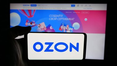 Stuttgart, Almanya - 05-27-2025: İnternet sayfasındaki ekranda Rus e-ticaret şirketi Özon 'un (Özon.ru) logosunu elinde tutan kişi. Telefon ekranına odaklan.