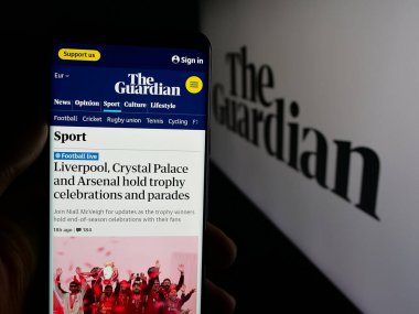 Stuttgart, Almanya - 05-27-2025: İngiliz gazete şirketi The Guardian 'ın logo önündeki web sayfası ile cep telefonu tutan kişi. Telefon ekranının merkezine odaklan.