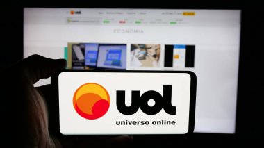 Stuttgart, Almanya - 05-27-2025: İnternet sayfası önünde ekranda Brezilya web platformu Universo Online (UOL) logosu bulunan cep telefonu sahibi kişi. Telefon ekranına odaklan.
