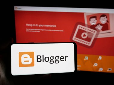 Stuttgart, Almanya - 05-29-2025: İçerik yönetim sistemi şirketi Blogger.com 'un logosunun bulunduğu akıllı telefonu web sitesinin önünde ekranda tutan kişi. Telefon ekranına odaklan.