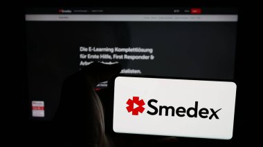 Stuttgart, Almanya - 05-29-2025: İsviçreli e-öğrenim şirketi Smedex AG 'nin logosunu taşıyan cep telefonu sahibi kişi web sayfasının önünde ekranda. Telefon ekranına odaklan.