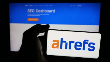 Stuttgart, Almanya - 05-29-2025: SEO araç şirketi Ahrefs Pte 'nin logosuna sahip cep telefonu sahibi kişi. Ltd. Web sayfasının önünde ekranda. Telefon ekranına odaklan.
