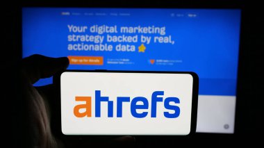 Stuttgart, Almanya - 05-29-2025: SEO araç şirketi Ahrefs Pte 'nin logosuna sahip cep telefonu sahibi kişi. Ltd. Web sayfasının önünde ekranda. Telefon ekranına odaklan.