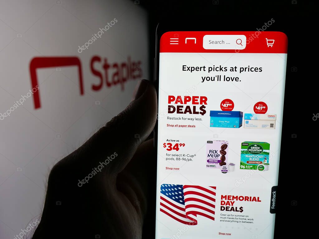 Stuttgart, Germany - 05-26-2025: Person holding cellphone with webpage of US office supply retail company Staples Inc. on screen in front of logo. Focus on center of phone display.