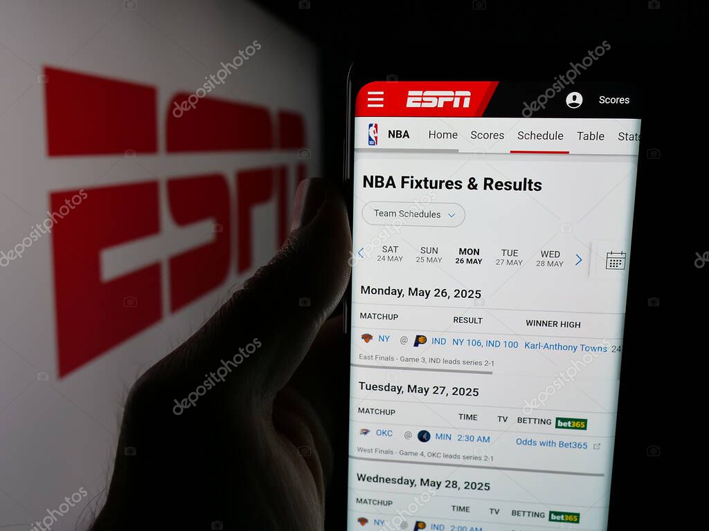 Stuttgart, Germany - 05-27-2025: Person holding cellphone with webpage of US cable sports television channel ESPN on screen in front of logo. Focus on center of phone display.