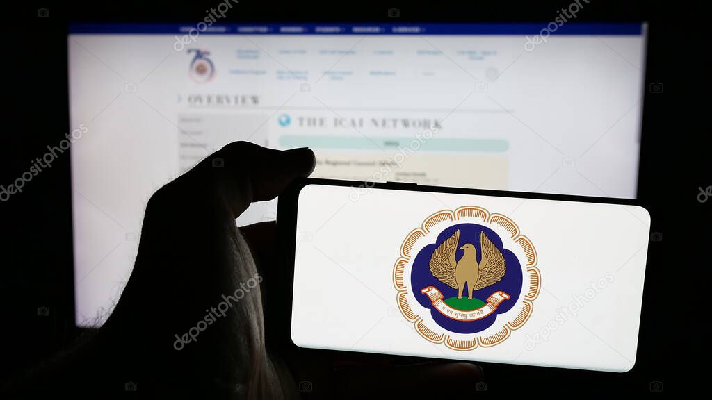 Stuttgart, Germany - 05-29-2025: Person holding mobile phone with logo of Institute of Chartered Accountants (ICAI) on screen in front of web page. Focus on phone display.