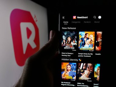 Stuttgart, Almanya - 05-31-2025: Kısa video uygulama şirketi ReelShort 'un web sayfası olan akıllı telefonu logo önünde ekranda tutan kişi. Telefon ekranının merkezine odaklan.