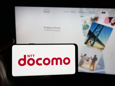 Stuttgart, Almanya - 05-31-2025: İnternet sitesi önünde üzerinde telekomünikasyon şirketi NTT Docomo Inc. 'nin logosu bulunan akıllı telefon sahibi kişi. Telefon ekranına odaklan.