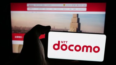 Stuttgart, Almanya - 05-31-2025: İnternet sayfası önünde üzerinde telekomünikasyon şirketi NTT Docomo Inc. logosu olan cep telefonu sahibi kişi. Telefon ekranına odaklan.