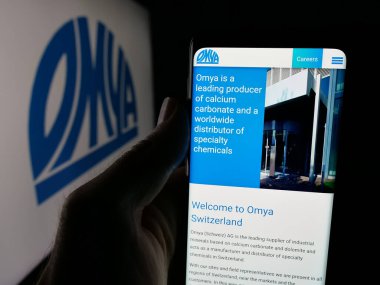 Stuttgart, Almanya - 05-31-2025: İsviçreli sanayi mineralleri şirketi Omya AG 'nin web sayfası ile logo önünde cep telefonu tutan kişi. Telefon ekranının merkezine odaklan.