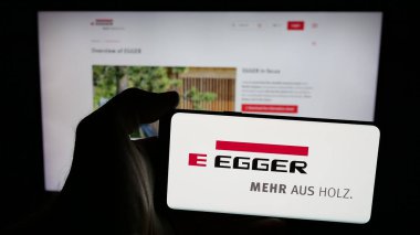 Stuttgart, Almanya - 05-31-2025: Avusturyalı Egger Holzwerkstoffe GmbH logosuna sahip cep telefonu sahibi kişi web sayfasının önünde ekranda. Telefon ekranına odaklan.
